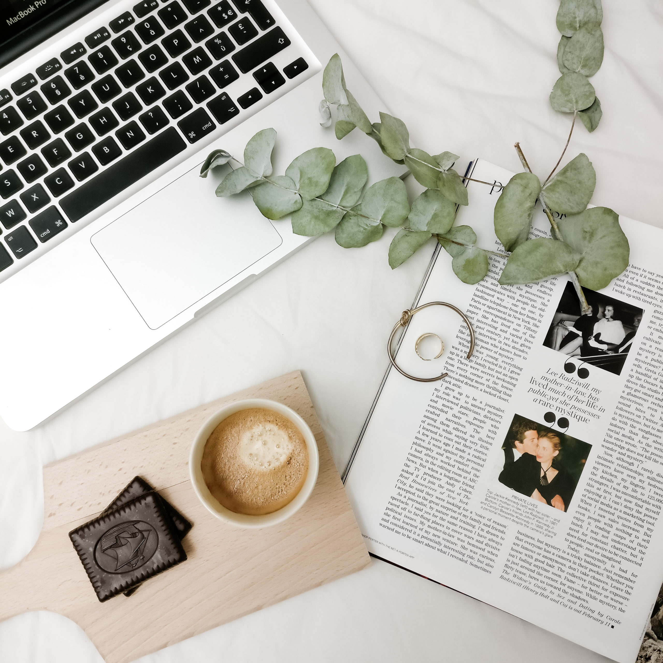 Sur l'image on voit un ordinateur portable ouvert, un journal posé à côté ainsi qu'une tasse de café