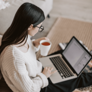 Femme assise devant son ordinateur portable avec une tasse de thé à la main