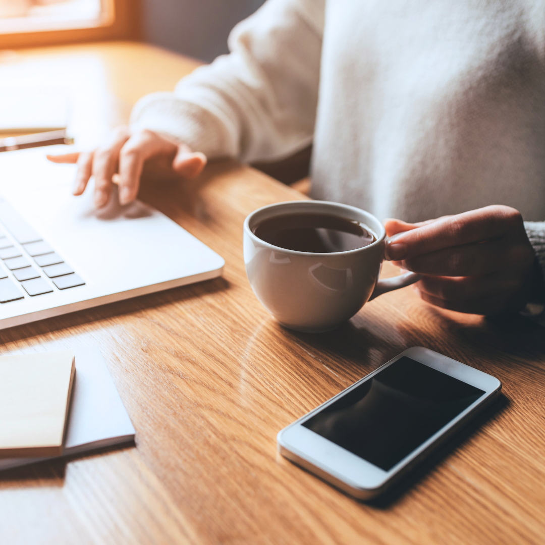 Femme assise à un bureau avec une tasse de café à la main et un ordinateur ouvert à côté d'elle